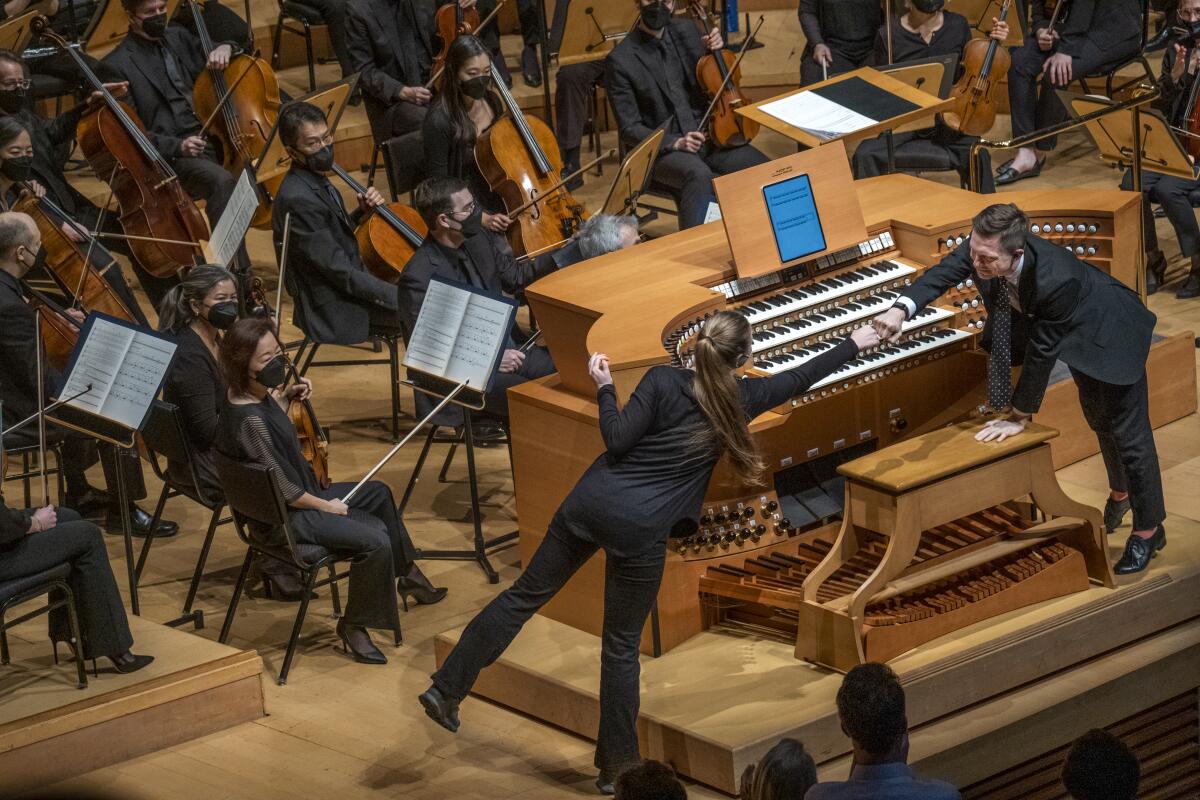 A man and a woman fist-bump in front of a seated orchestra.