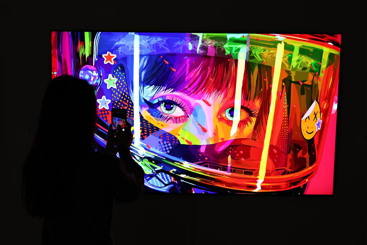 A person in a dark room stands in front of a brightly colored image of a person's face. 