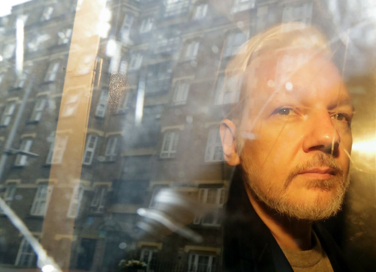 WikiLeaks founder Julian Assange seen through a window reflecting buildings.