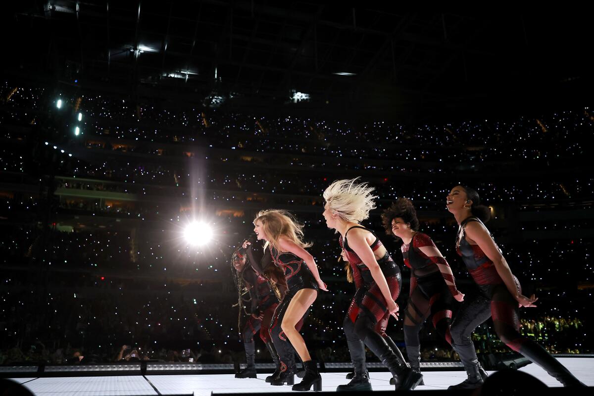 Taylor Swift and dancers lean forward on stage at SoFi Stadium in front of the crowd. 