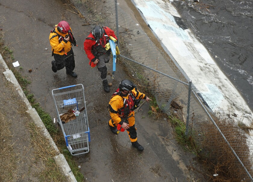 Members of the San Diego Lifeguard River Rescue Team walk along a flood control channel along I-15 in Mission Valley.