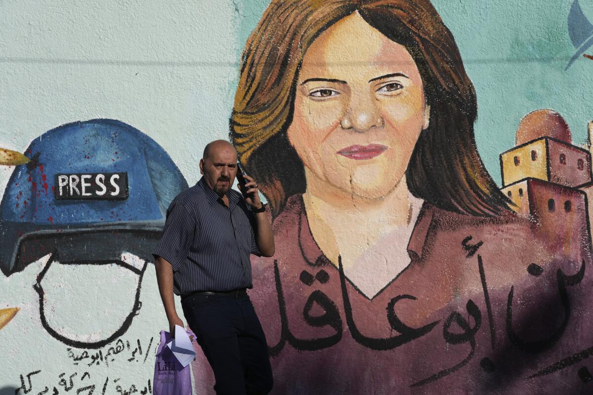 A man speaks on his phone near a mural of a woman with brown hair, Arabic script and a blue helmet with the word "Press" 