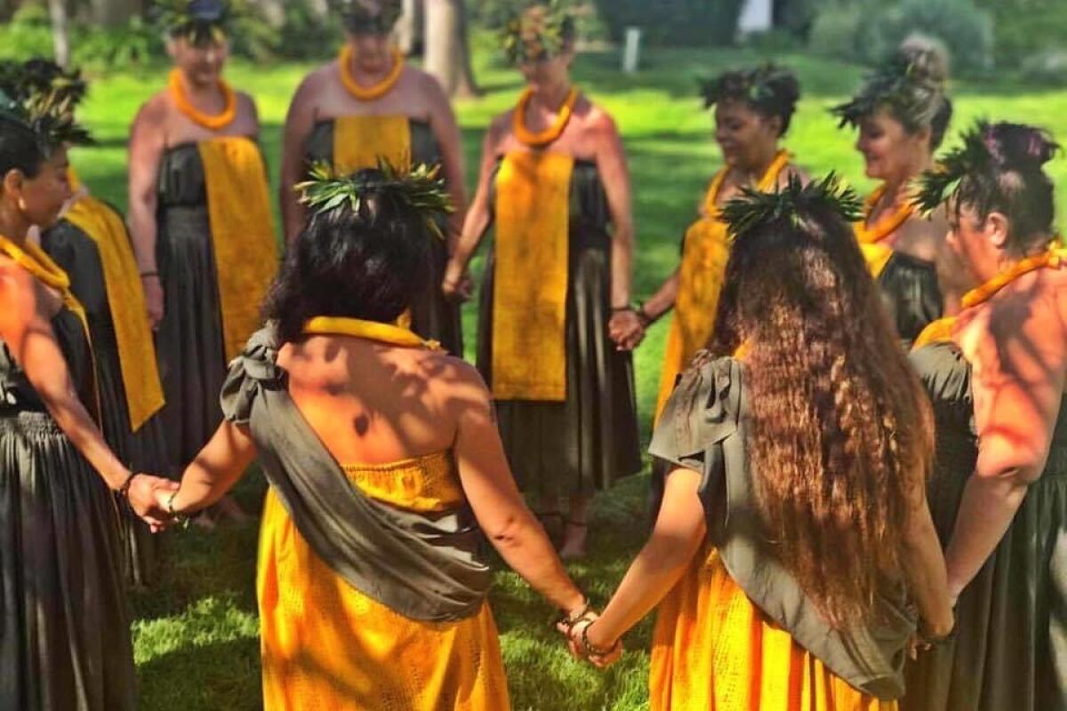 Members of the Hula Group, wearing traditional hula garb, stand holding hands in a prayer circle.