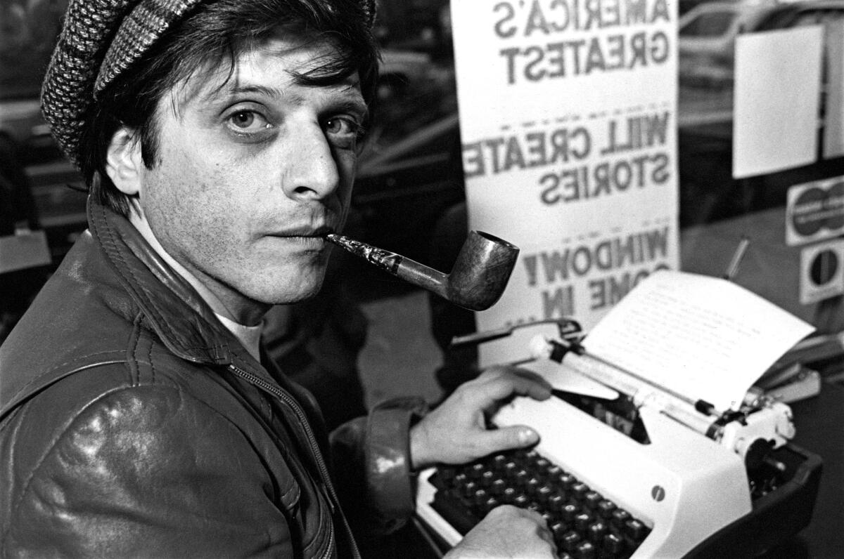 Harlan Ellison, with a pipe in his mouth, looks into the camera as he hits keys on a typewriter.