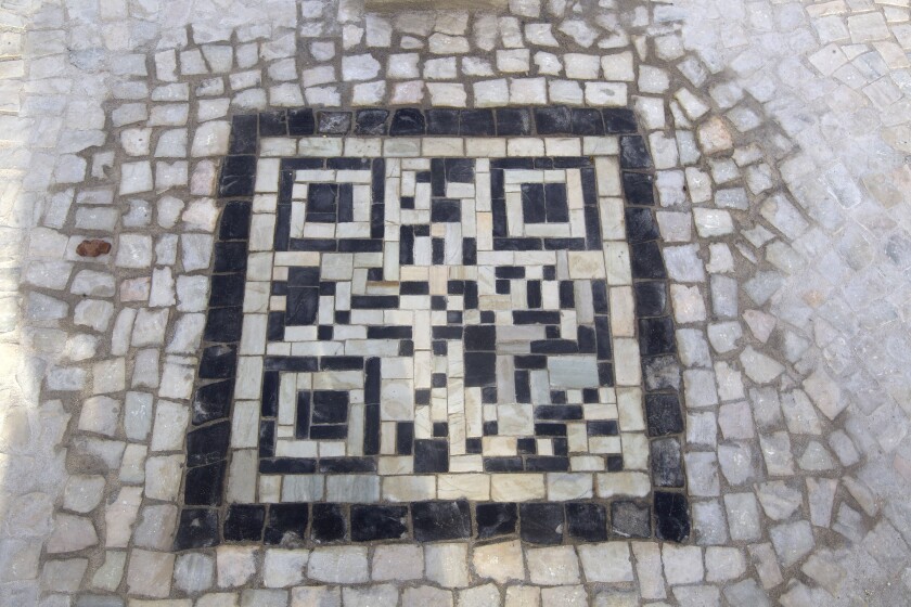 An overhead photograph shows a QR code made out of mosaic tile in a sidewalk.