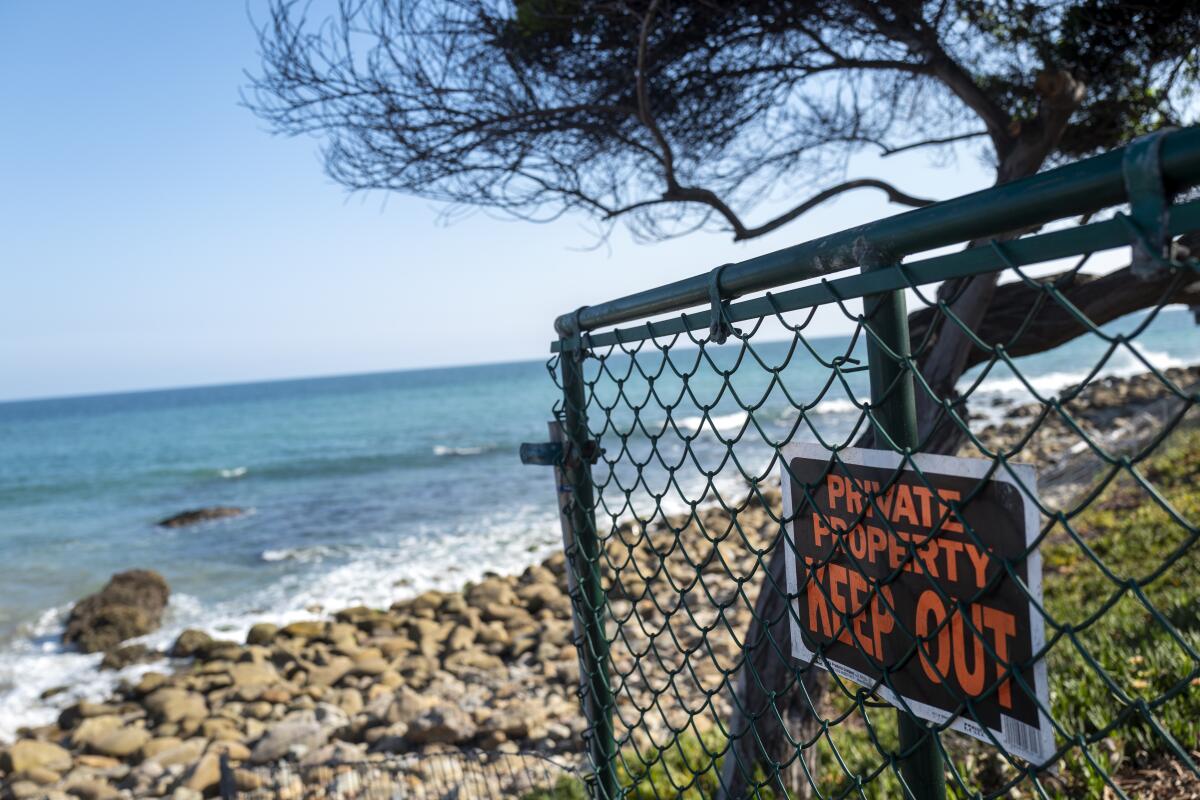 A sign reading "Private Property, Keep Out" is attached to an open gate on a beach.