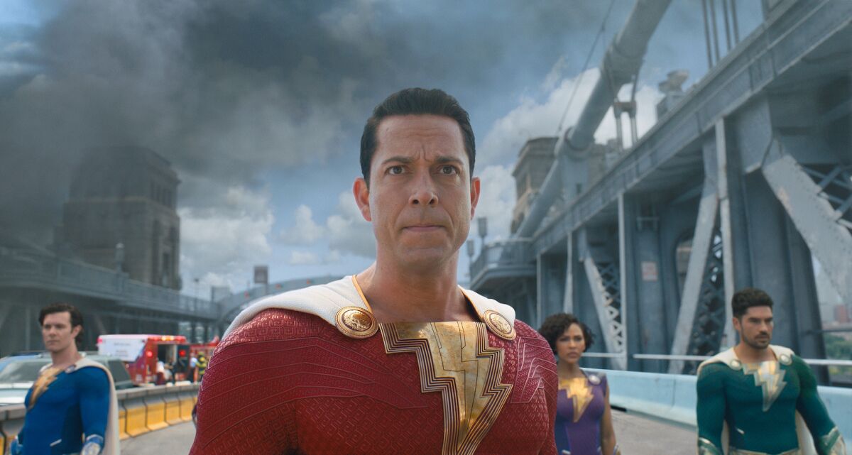 Three men and a woman in superhero outfits on a bridge in the movie "Shazam! Fury of the Gods."