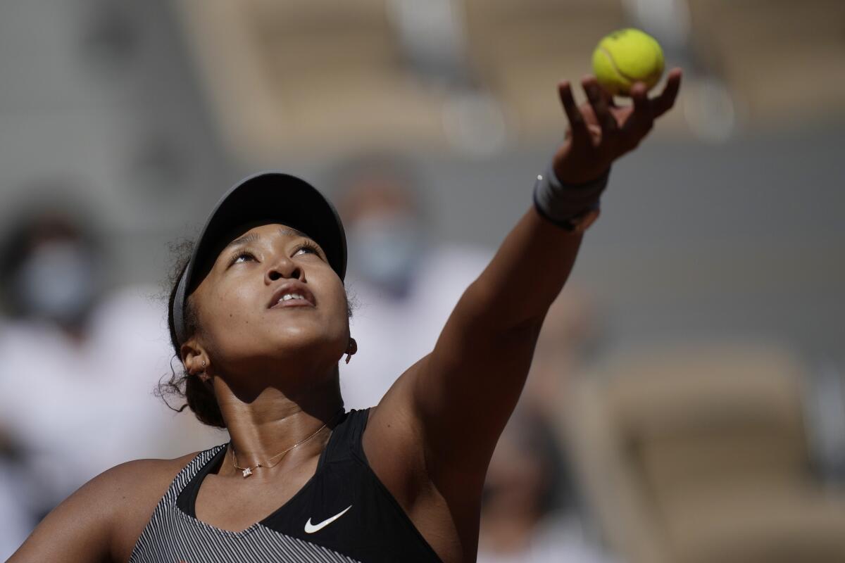 A woman in a visor lifting a tennis ball into the air.
