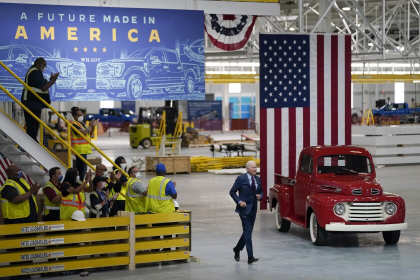 People clap as President Biden walks past them, next to a red pickup truck and U.S. flag 
