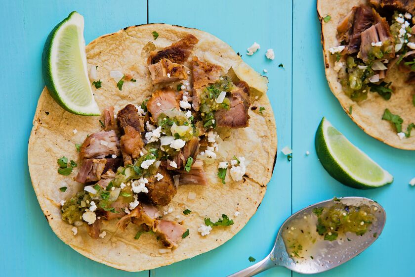 Two carnitas tacos garnished with salsa verde, cheese and cilantro.