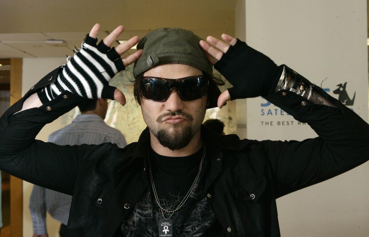 A man wearing dark sunglasses and fingerless gloves with his hands framing his face