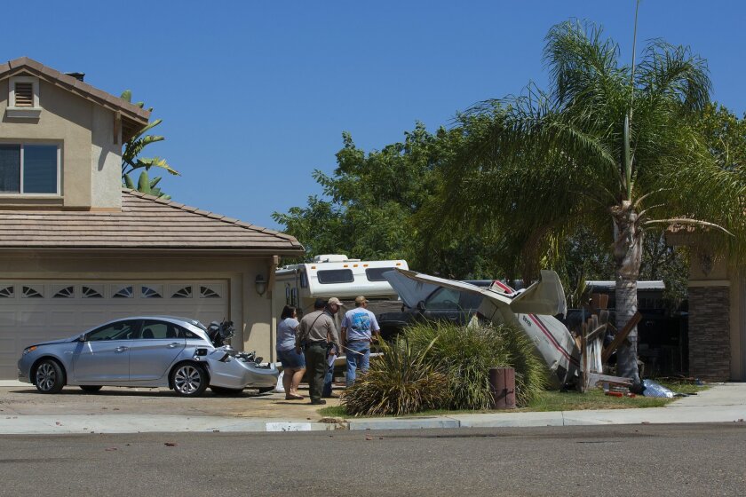 Neighbors look over a small aircraft that crashed into driveway of a home in Santee on Corte De La Donna. The aircraft struck the roof top, and a 4-door sedan before crashing on the driveway of one of the homes in the small cul de sac.