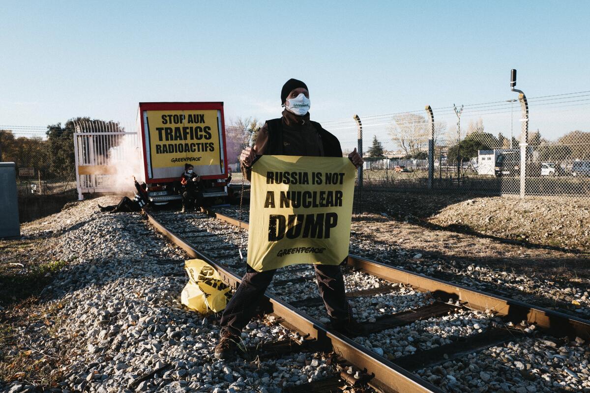 A Greenpeace activist holds a banner during an attempt to block a railway access in southern France where Greenpeace say a convoy of reprocessed uranium is due to leave to be exported to Russia, in Pierrelate, southern France, Tuesday, Nov. 16, 2021. The railway access is located in Pierrelatte, just outside the Orano plant where radioactive material is processed and stored. (Mait Baldi/ Greenpeace via AP)