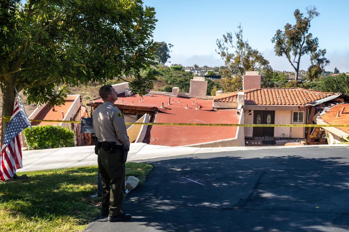 A Los Angeles County sheriff's deputy stands in front of collapsed houses on Peartree Lane in Rolling Hills Estates