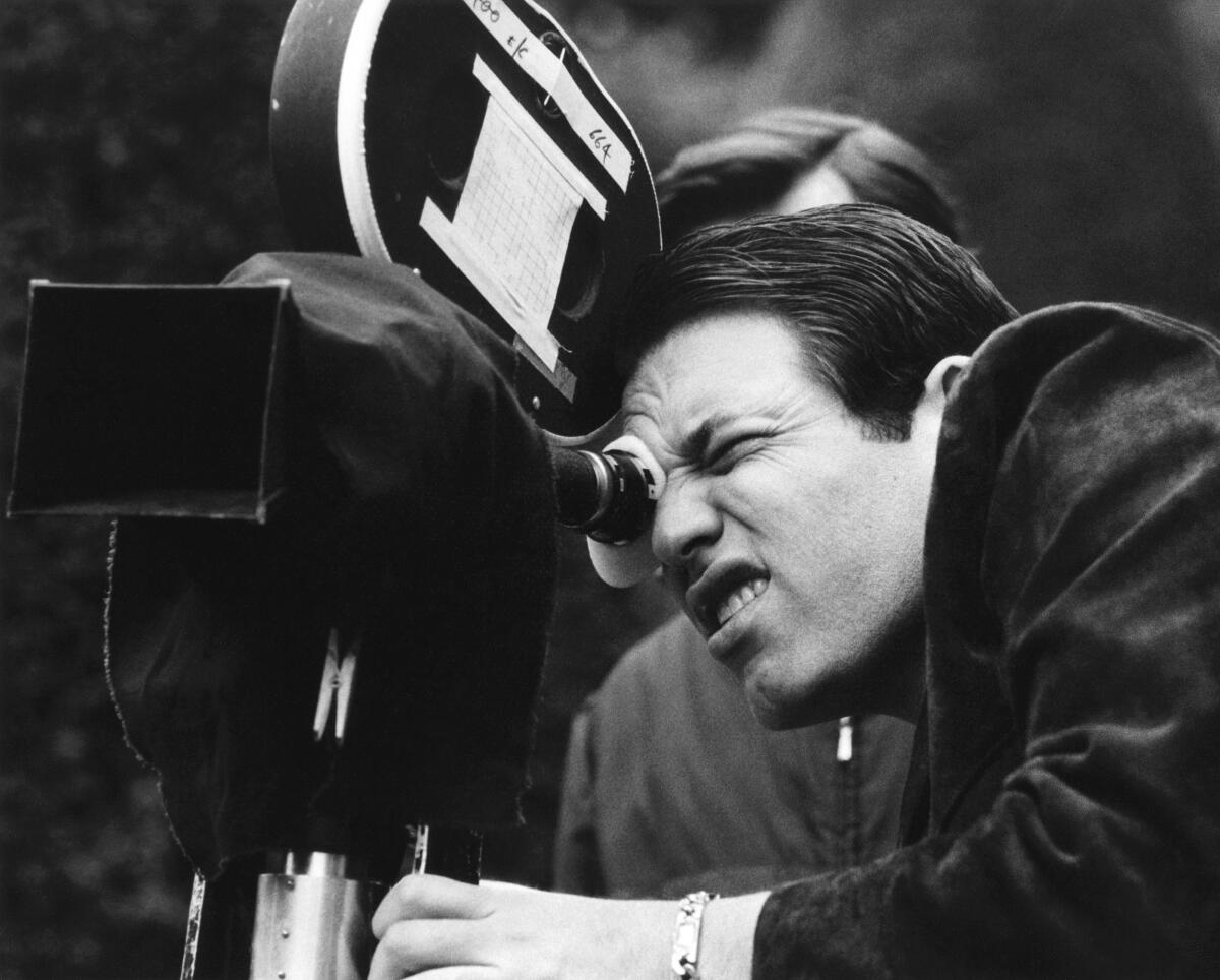 A man squints into the viewfinder of a film camera.