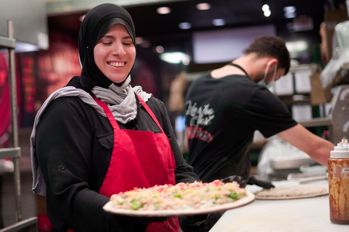 A woman in hijab prepares to put a pizza into the oven at Big Al's in Maywood.