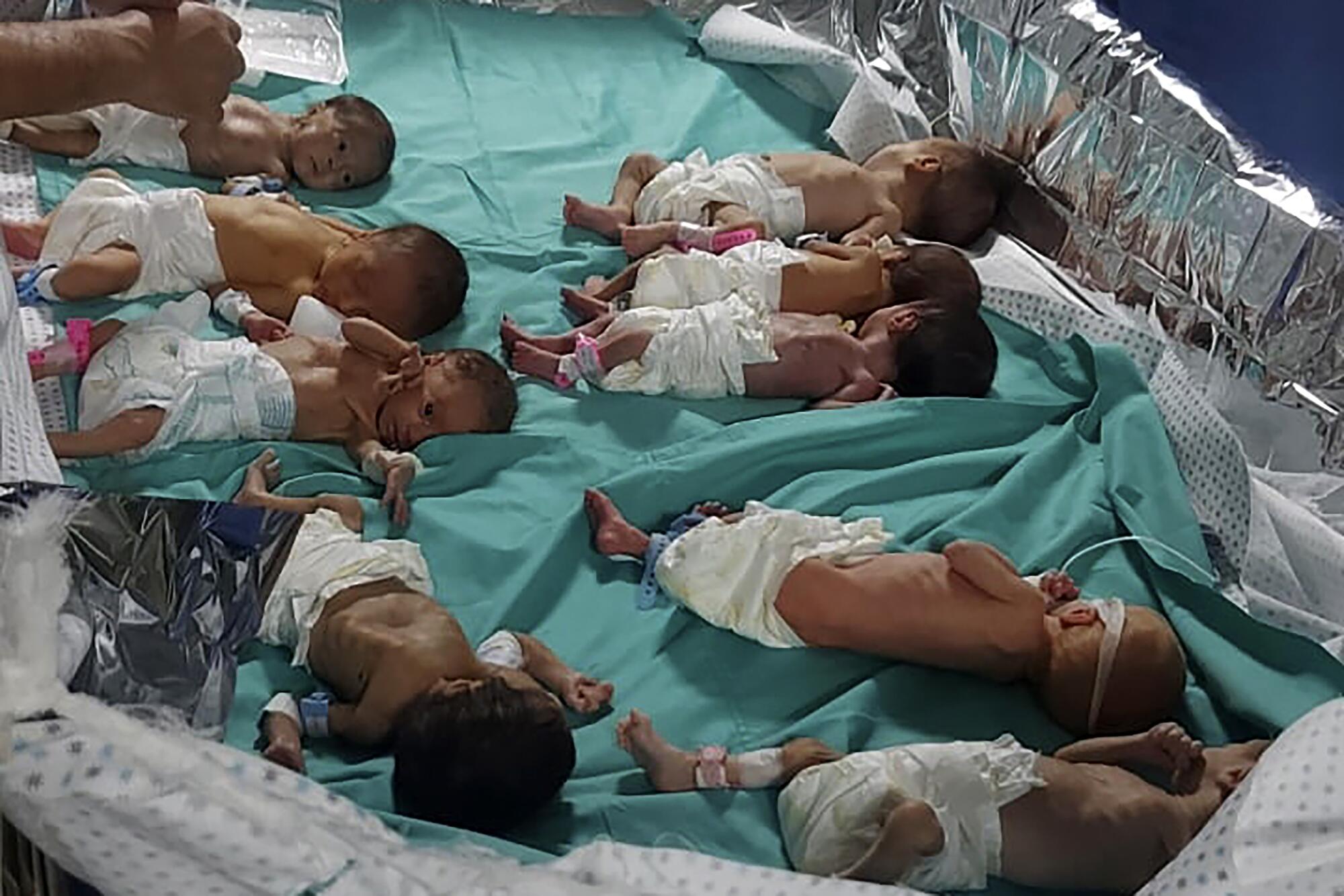 A group of babies in diapers lie near one another on a blue cloth 