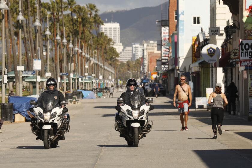 LOS ANGELES, CA - MARCH 23, 2020 LAPD officers on patrol with fewer people than usual walk on the Venice Boardwalk Monday morning in light of the Coronavirus threat after Mayor Eric Garcetti on Sunday admonished Angelenos who haven't taken orders to practice social distancing seriously, announcing the closure of the city's golf courses, parking lots at Venice Beach and organized group sports at city parks as they have continued to attract thongs of people. (Al Seib / Los Angeles Times)