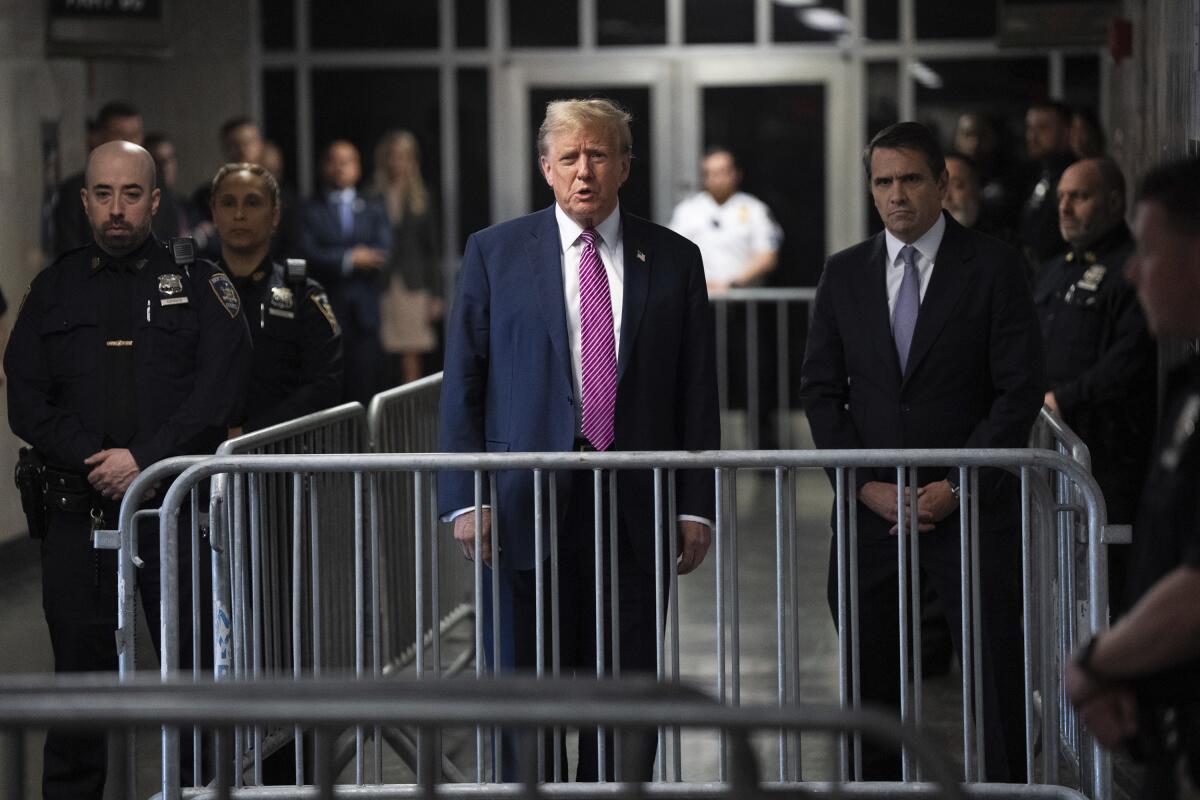 Donald Trump fala com a mídia por trás de barreiras no corredor de um tribunal criminal de Manhattan. 