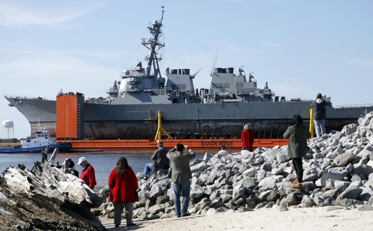 A transport vessel carries the damaged Fitzgerald while onlookers watch from land