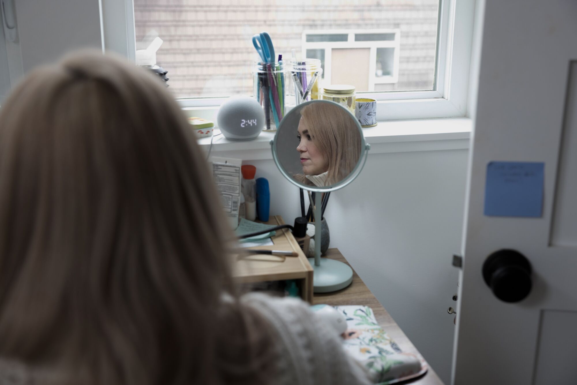 A woman sitting at a vanity table, her face reflected in a mirror