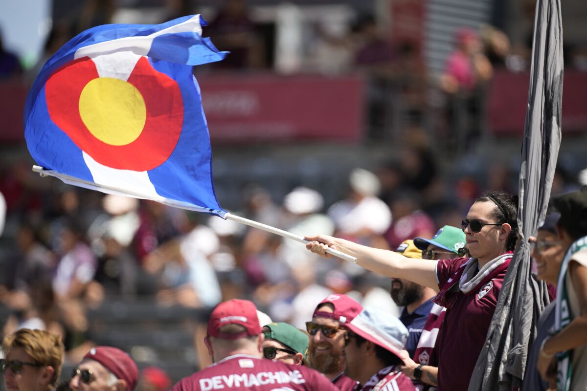 A fFan waves a Colorado state flag while cheering for the Colorado Rapids in the first half of an MLS soccer match against Los Angeles FC, Saturday, May 14, 2022, in Commerce City, Colo. (AP Photo/David Zalubowski)