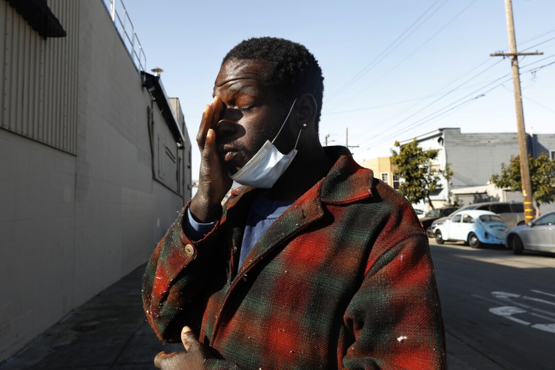 A person in a plaid jacket pauses to rub his eyes