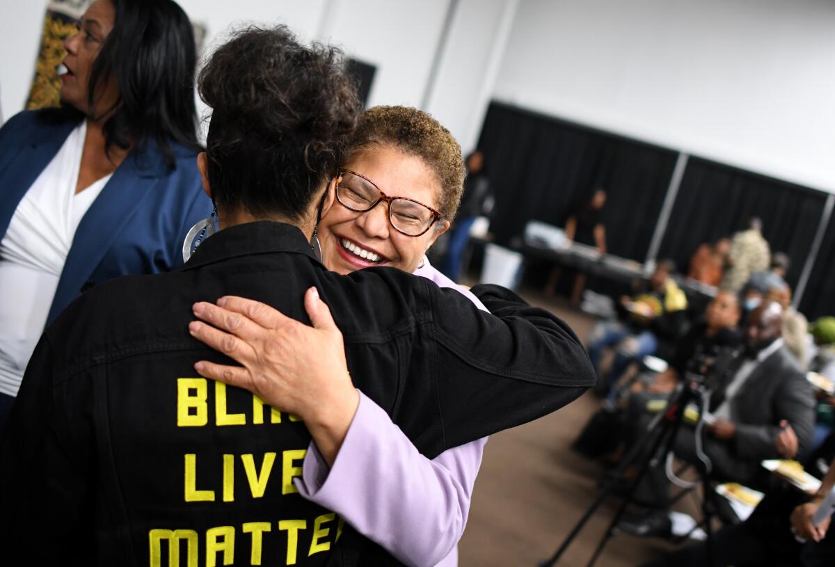 Mayor Karen Bass, in lavender blazer, hugs an activist wearing a jacket with "Black Lives Matter" in capital lettering