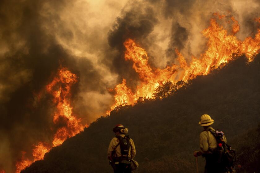 Flames from the River Fire crest a ridge as firefighters Ian Johnson, right, and Capt. Mike Campbell protects a home in Salinas, Calif., on Monday, Aug. 17, 2020. Fire crews across the region scrambled to contain dozens of blazes sparked by lightning strikes as a statewide heatwave continues. (AP Photo/Noah Berger)