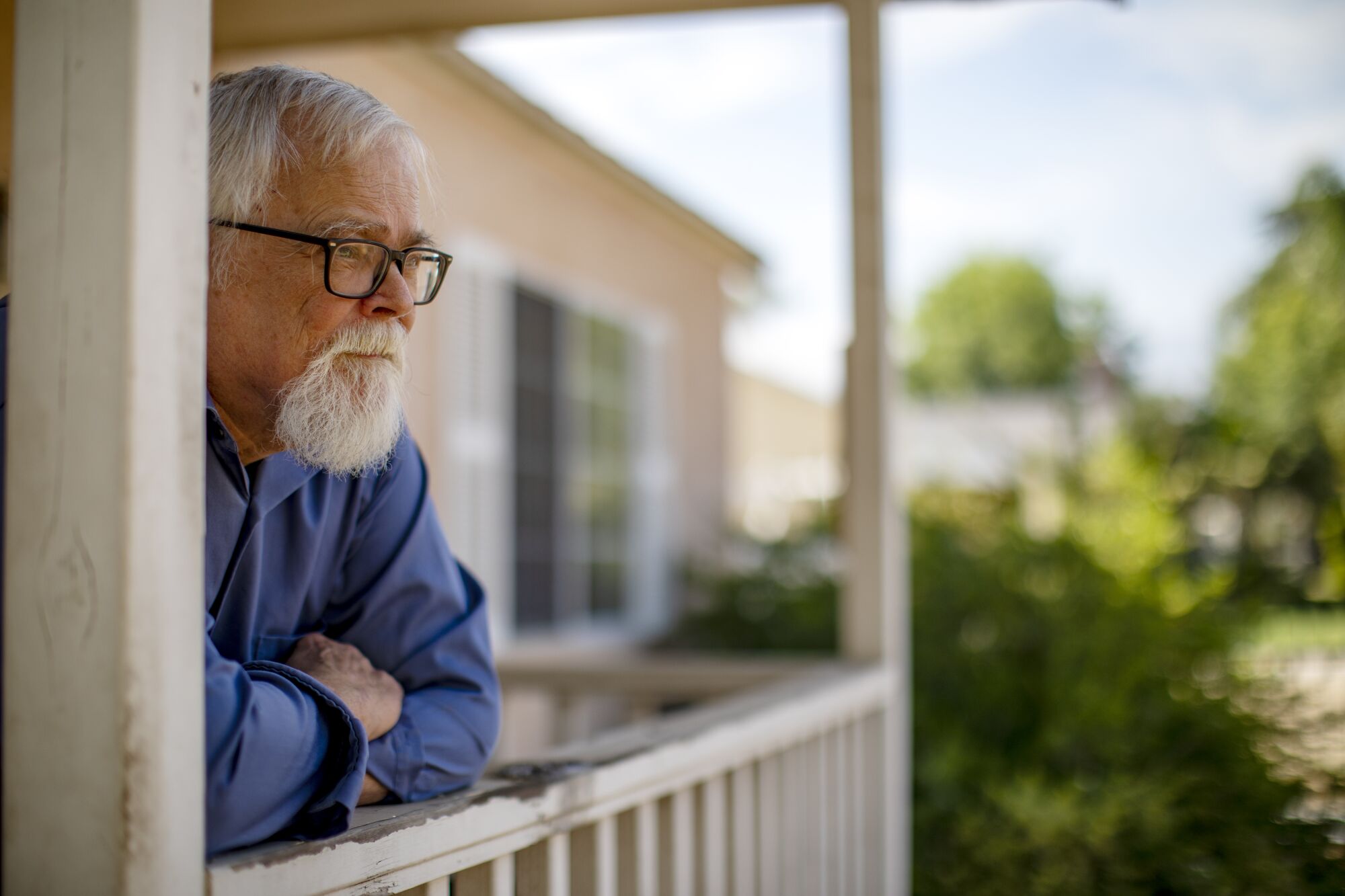 A man leans against a low wooden fence around a home's patio.
