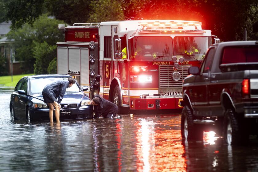 Dos personas atan un cabo a un auto varado en una calle anegada debido a las fuertes lluvias de la tormenta tropical Debby, el 5 de agosto de 2024, en Savannah, Georgia. (AP Foto/Stephen B. Morton)