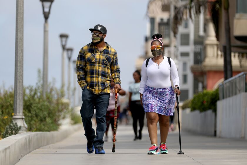 MANHATTAN BEACH, CA - JULY 03: Anthony Mitchell, left, and Anissa Randle, of Los Angeles, take a walk along The Strand as it remains open to joggers and pedestrians on Friday, July 3, 2020 in Manhattan Beach, CA. Los Angeles County Closes Beaches, Piers, Beach Parking Lots, Beach Bike Paths, and Beach Access Points for the Fourth of July Weekend due to Increased COVID-19 Cases. Closed from Friday, July 3rd at 12:00 A.M. thru Monday, July 6th at 5:00 A.M. (Gary Coronado / Los Angeles Times)