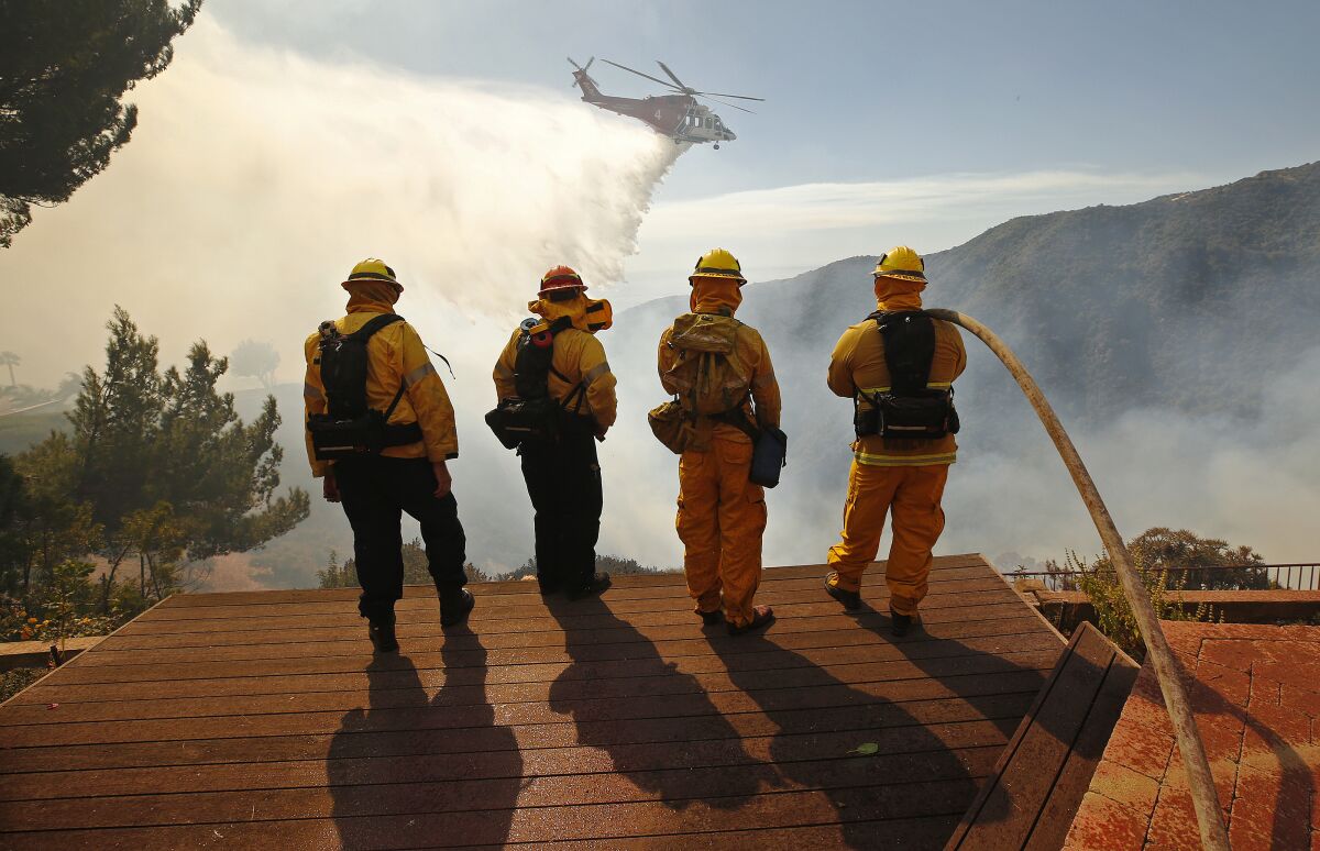 Firefighters watch a helicopter drop water on a brush fire in Pacific Palisades