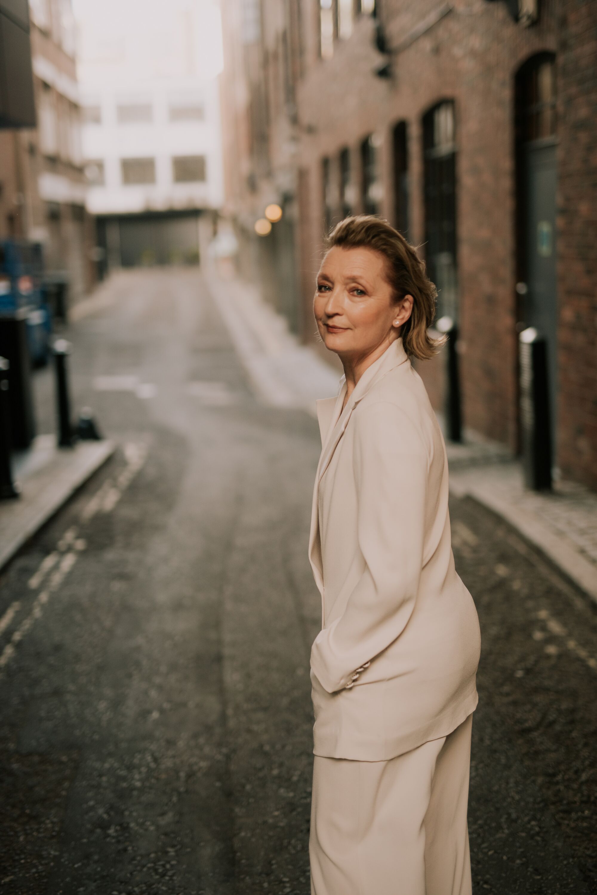 A woman in a white suit walks on a small road looking back