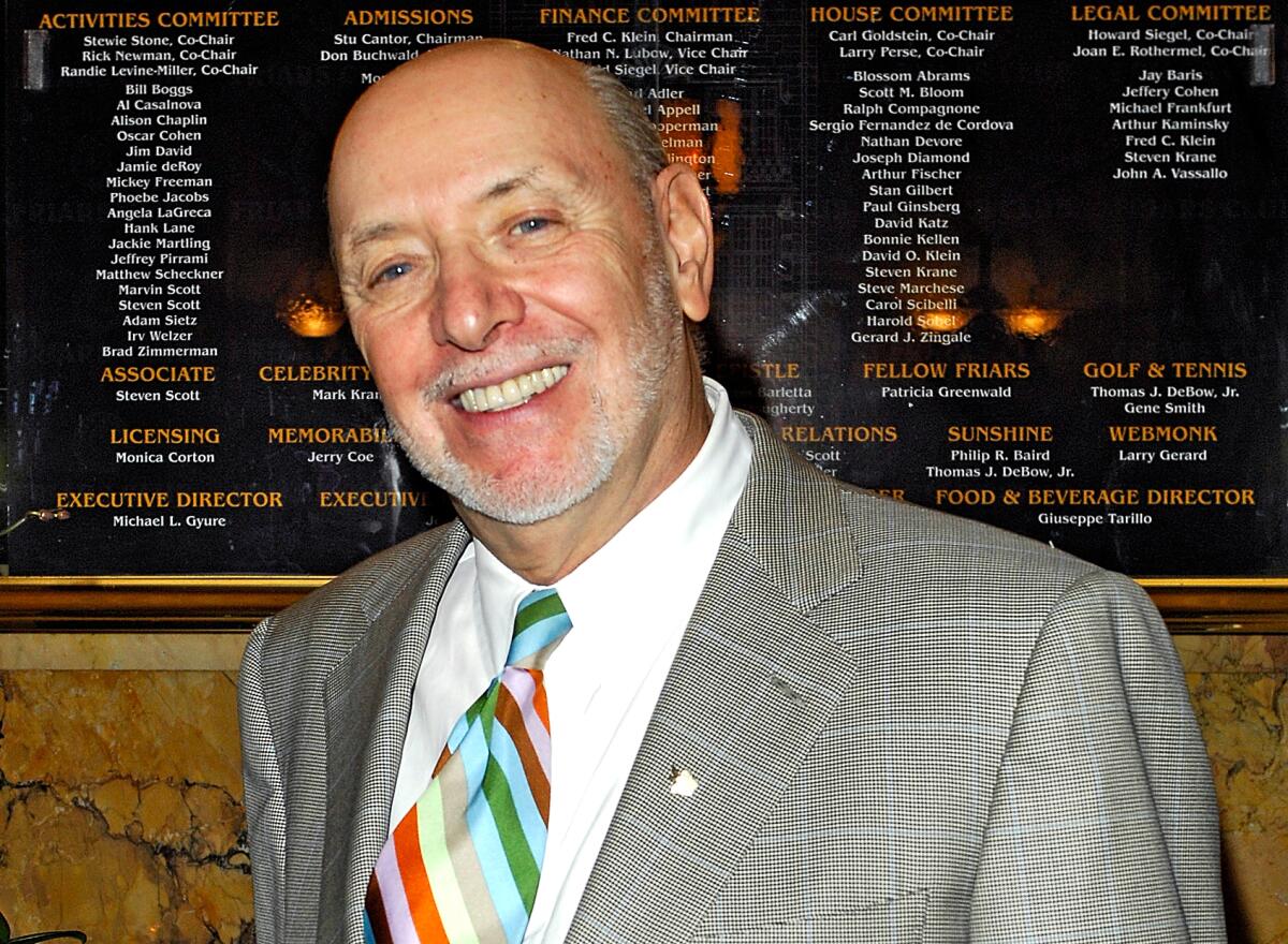 A man with a graying beard, wearing a gray sportcoat, white shirt and multicolored tie, tilts his head and smiles.