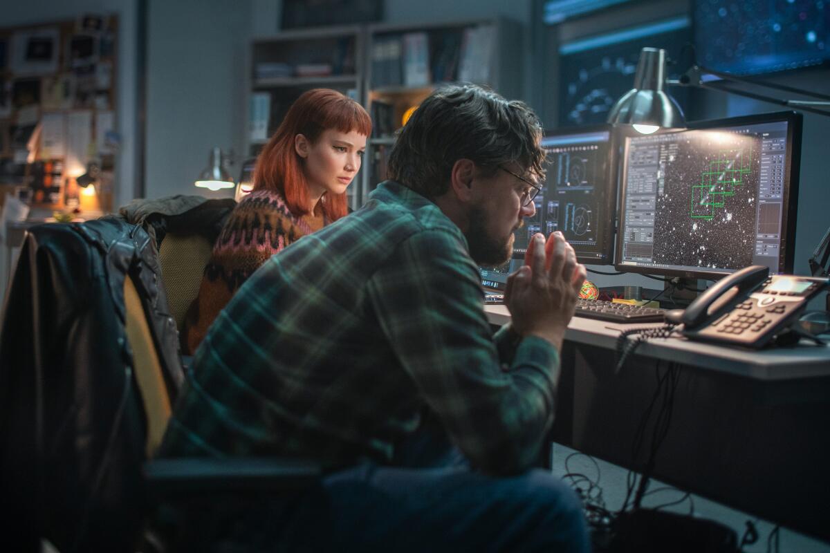 A woman and a man in an office hunching over computers and a landline telephone.