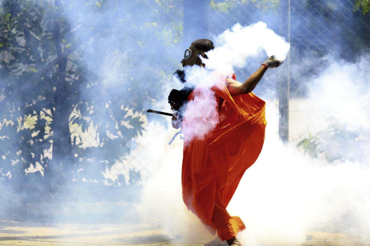 FILE - A man throws back a tear gas canister after it was fired by police to disperse protesters in Colombo, Sri Lanka, Saturday, July 9, 2022. The street protests that drove Sri Lanka’s President Gotabaya Rajapaksa from office last month brought together people from across the country’s diverse and sometimes warring ethno-religious groups: Tamils, Muslims, Christians and Sinhala Buddhists — including, unmistakably, the saffron-robed Buddhist monks who are fixtures of Sri Lanka’s political scene.(AP Photo/Amitha Thennakoon, File)