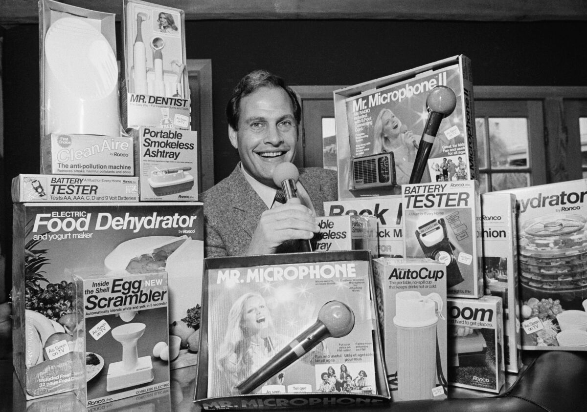 A man surrounded by boxes of such products as a food dehydrator, egg scrambler, microphone and smokeless ashtray