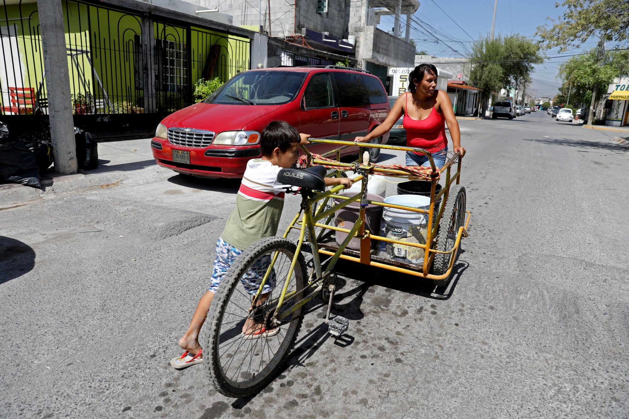 Su kovaları taşıyan bir üç tekerlekli bisiklet arabası olan bir kadın ve genç bir çocuk