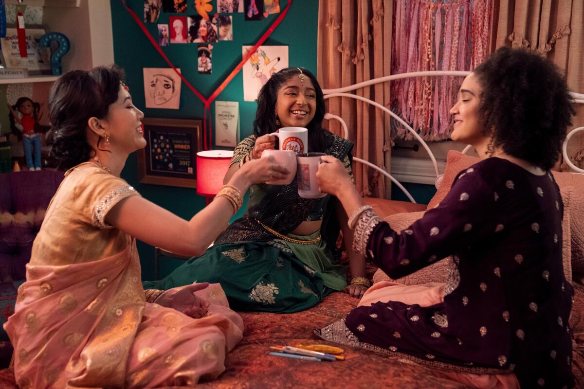Three teenage girls sitting on a bed toasting with coffee mugs.
