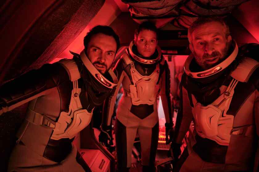 A woman and two men in spacesuits bathed in red light in the movie "Rubikon."