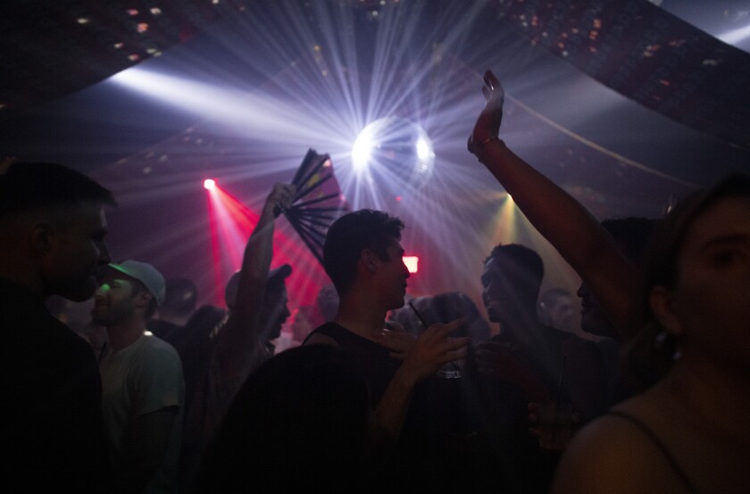 People dance in a dark club shot through with spotlights.