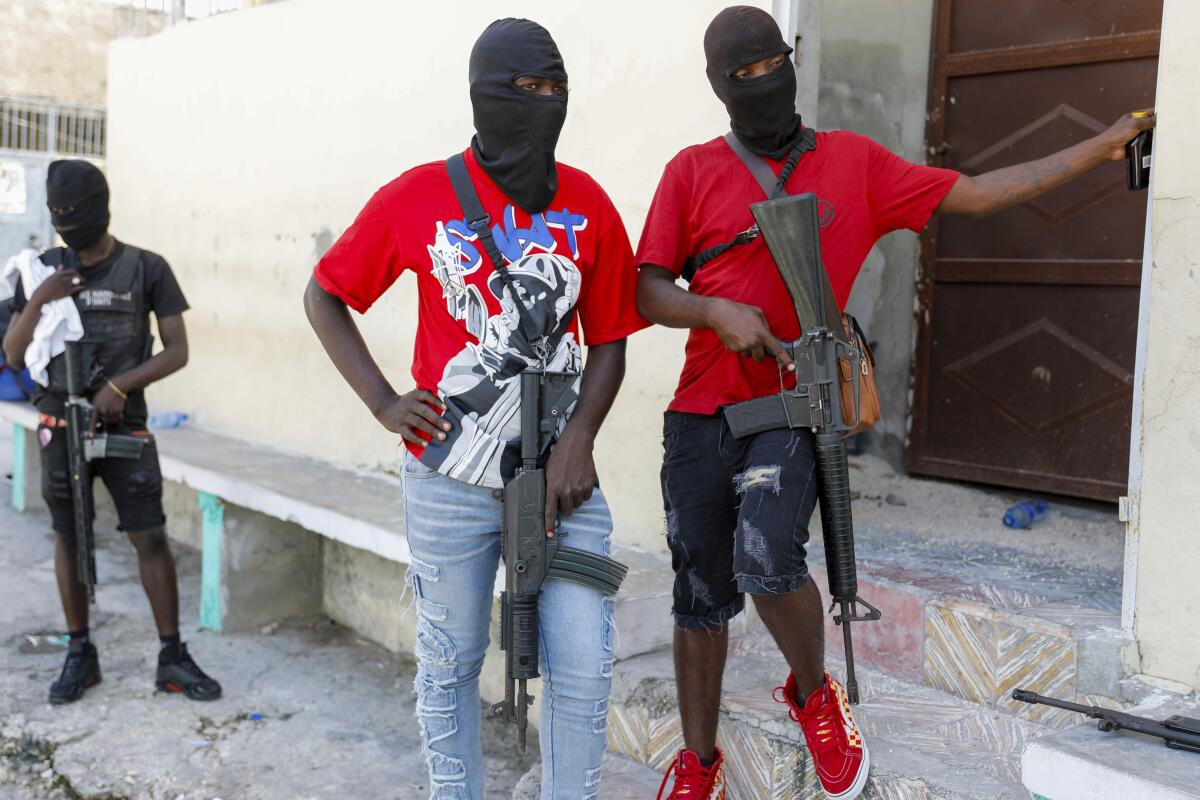 Three armed men in masks stand by a building in Haiti.