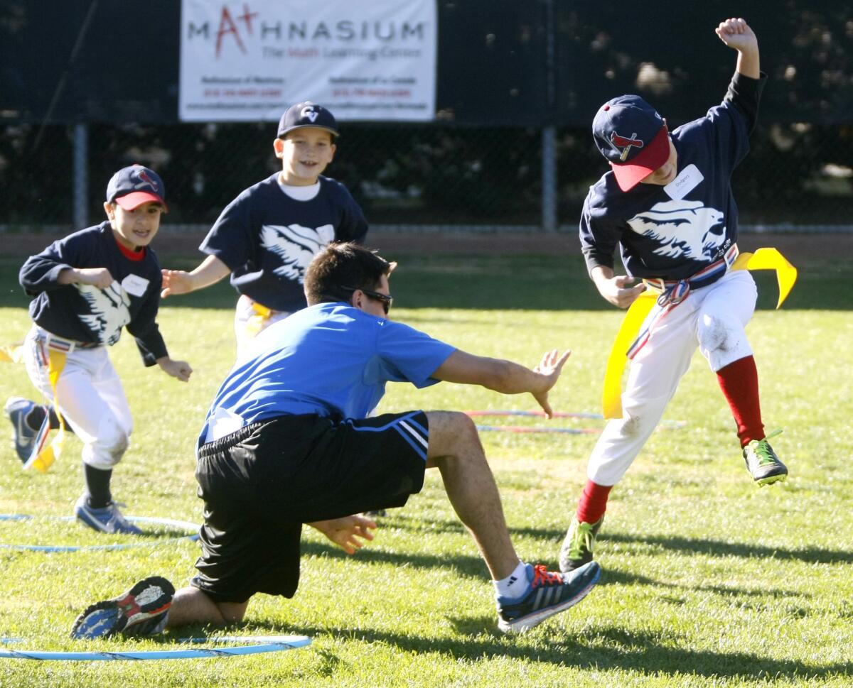 Nicholas Boghossian, 9, right, tries to avoid a coach's grab in flag tag at the annual Falcon Winter Baseball Camp at Stengel Field in Glendale on Thursday, Dec. 26, 2013. Crescenta Valley High School baseball coach Phil Torres runs the camp.
