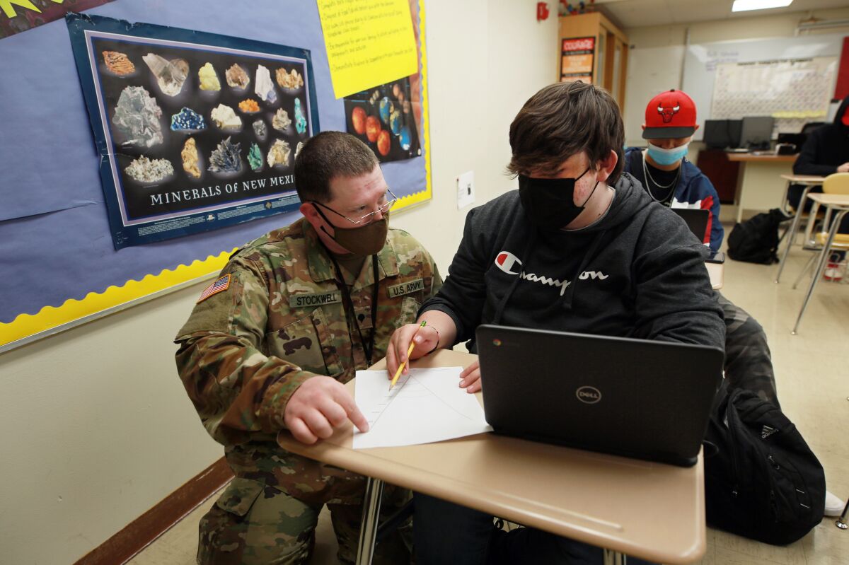 New Mexico Army National Guard specialist Michael Stockwell kneels while helping Alamogordo High School freshman Aiden Cruz with a geology assignment, at Alamogordo High School,Tuesday, Feb. 8, 2022, in Alamogordo, N.M. Dozens of National Guard Army and Air Force troops in New Mexico have been stepping in for an emergency unlike others they have responded to before: the shortage of teachers and school staff members that have tested the ability of schools nationwide to continue operating during the coronavirus pandemic. (AP Photo/Cedar Attanasio)