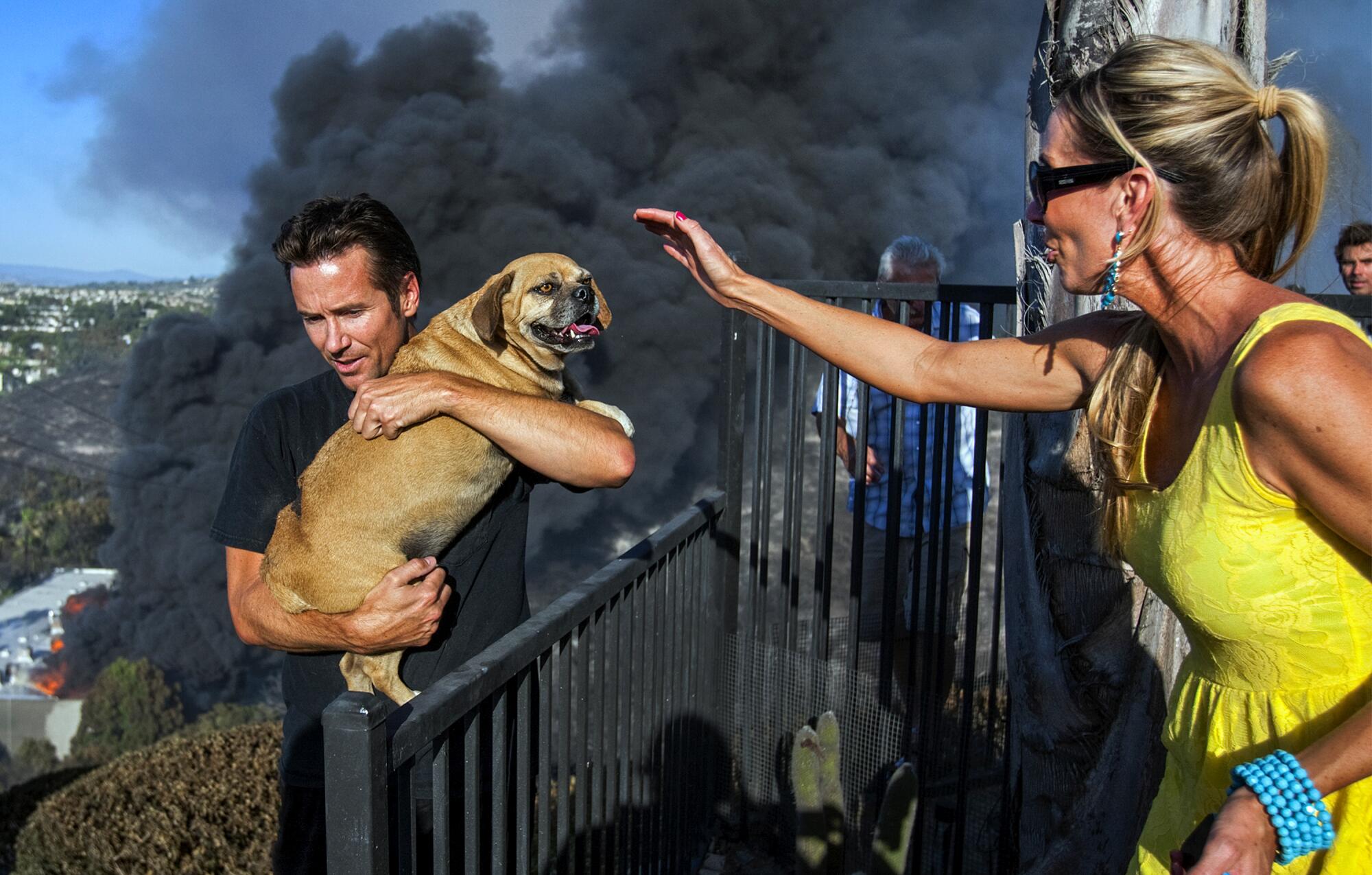 A woman reaches for a dog being carried from a burned home