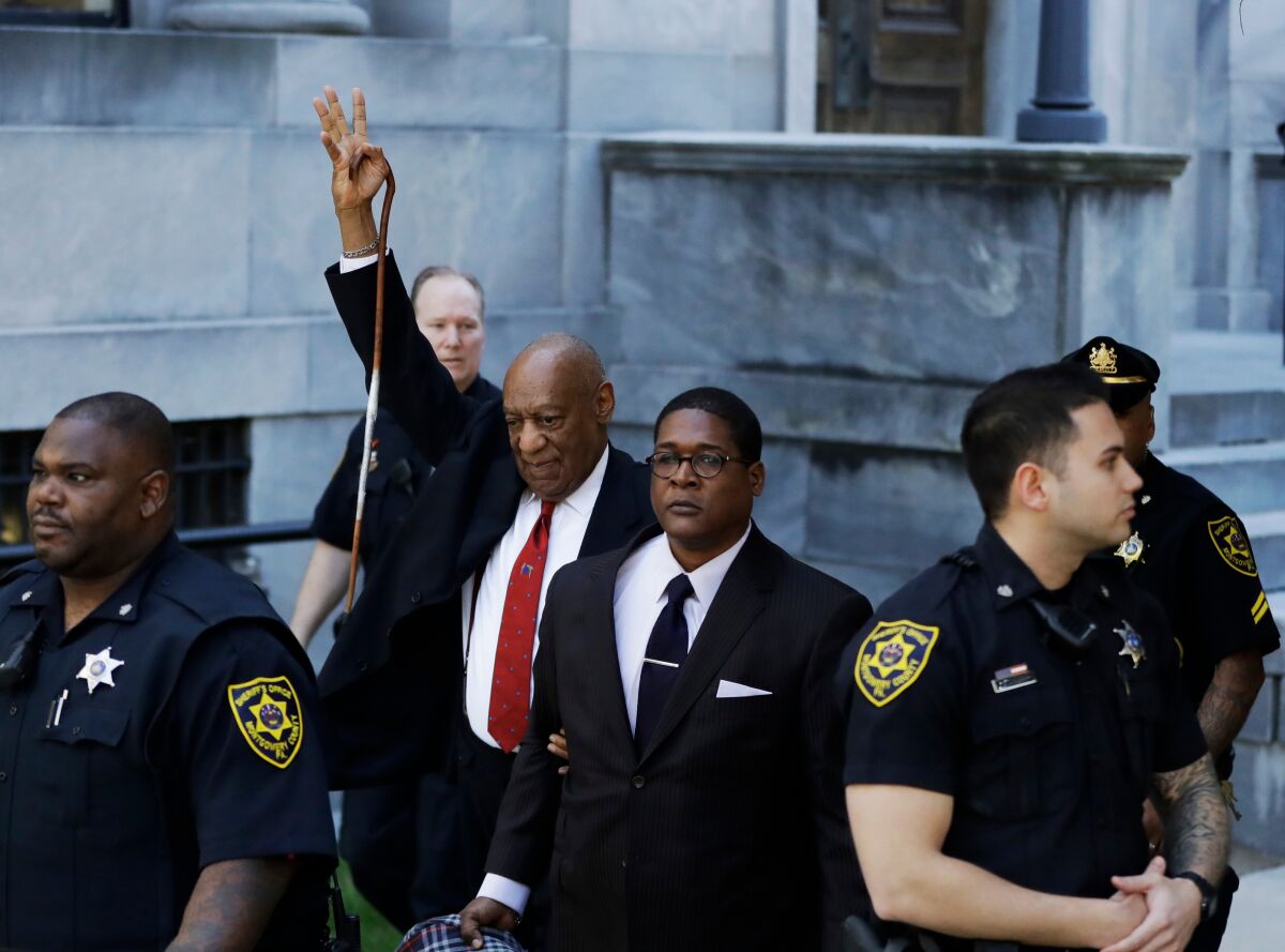 Bill Cosby raises his arm as he leaves a courthouse in 2018