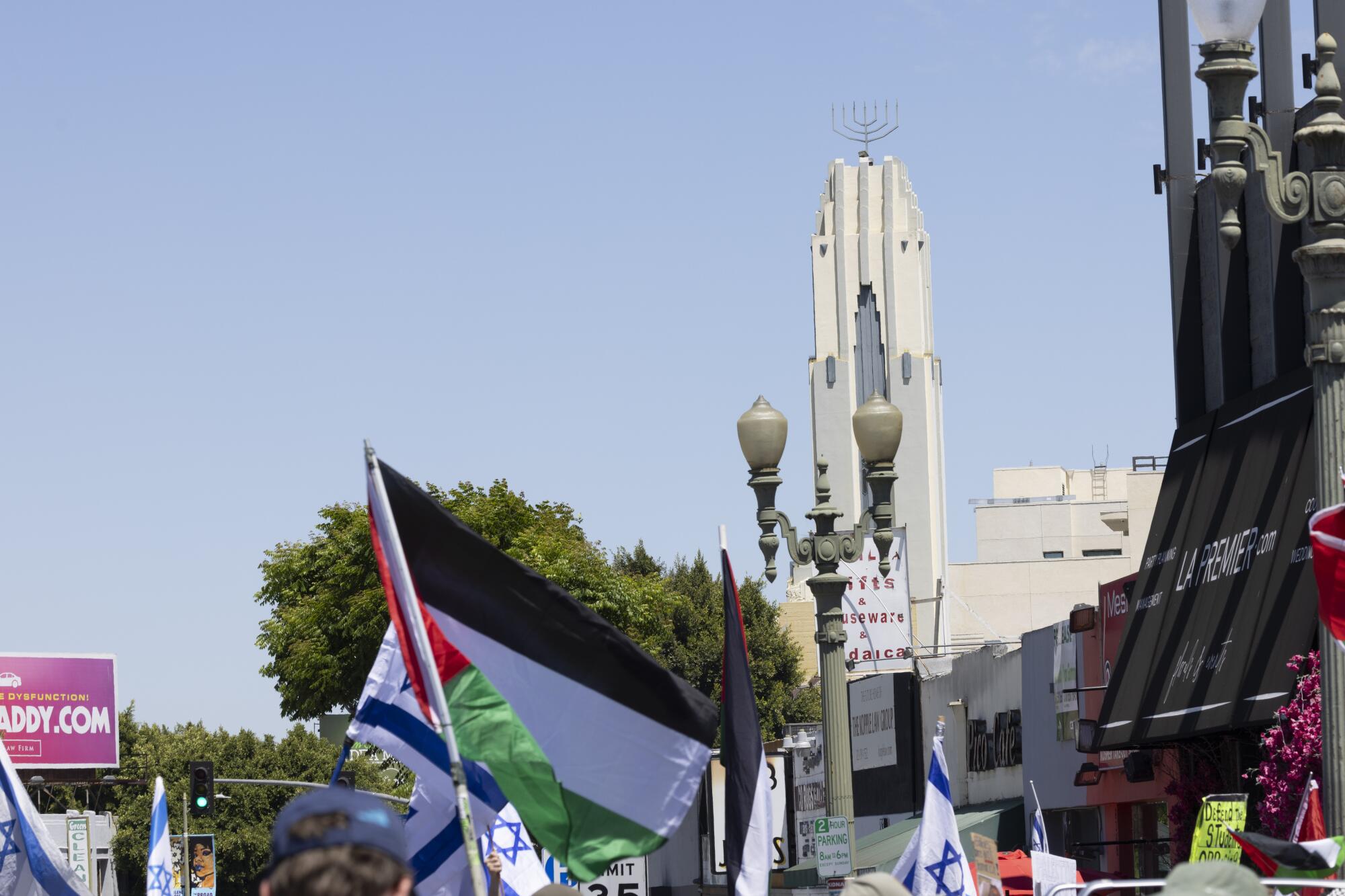 A synagogue in the background, with Israeli and Palestinian flags in the foreground