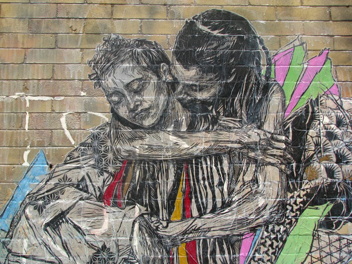 One figure embraces another in a print adhered to a brick wall by street artist Swoon.
