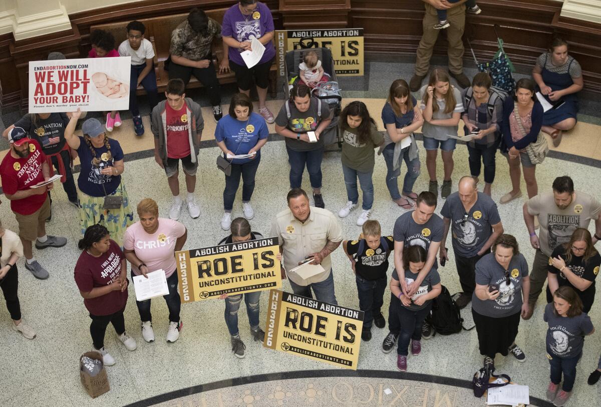 People with signs stand inside a building. Some signs say "Abolish abortion: Roe is unconstitutional."